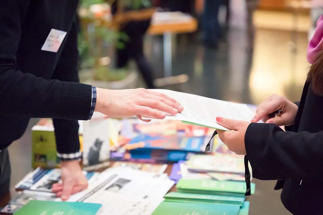 A cluttered trade show table with stacks of brochures and papers